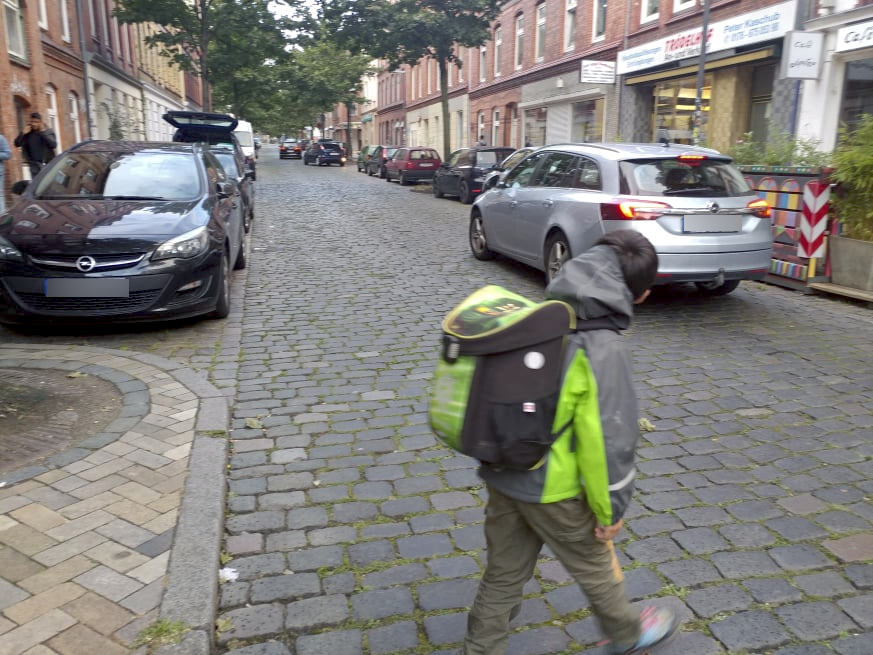 Ein Schulkind überquert eine Straße mit geparkten Autos auf beiden Seiten